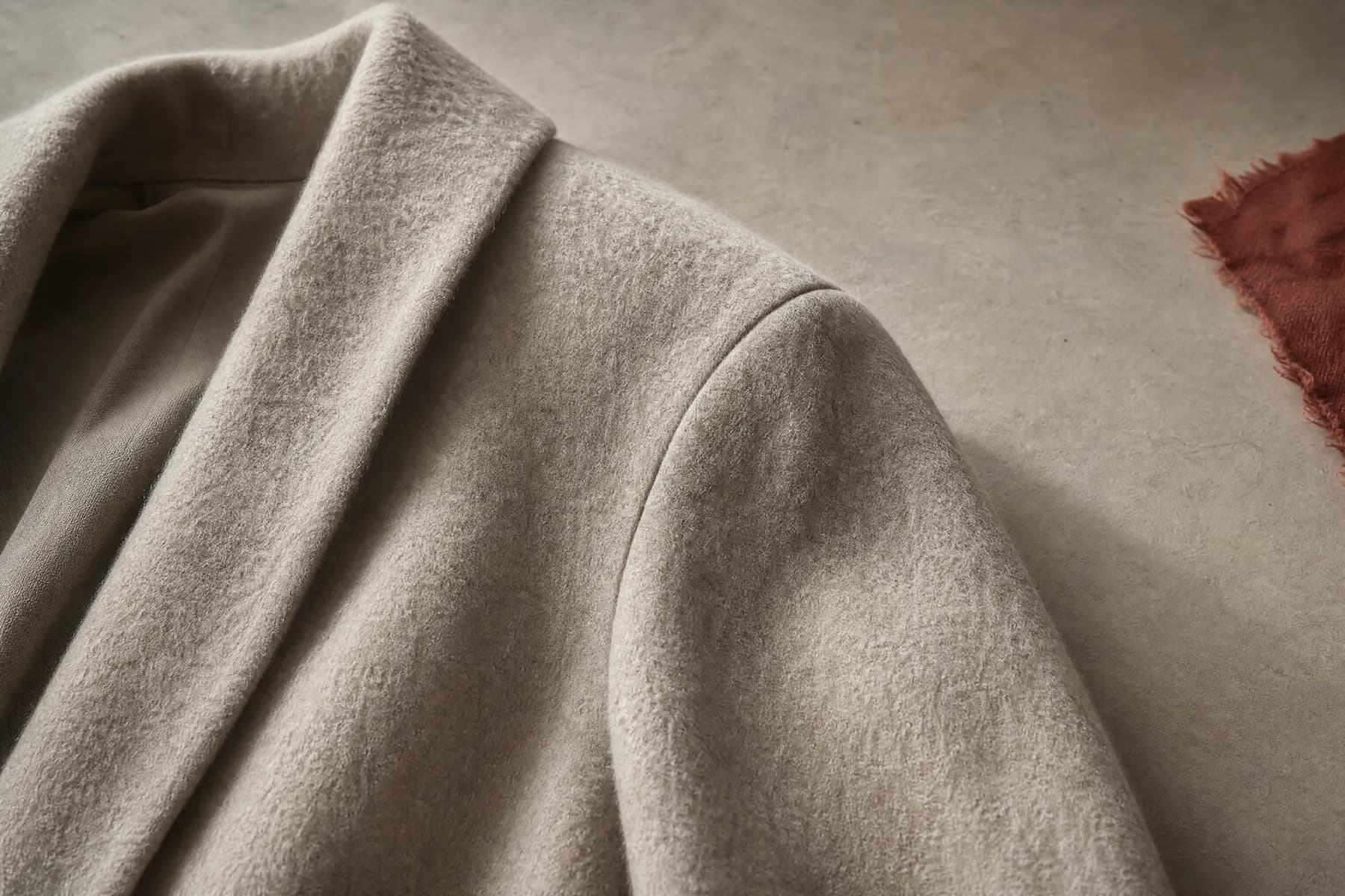 The shoulder and upper sleeve of a heavy wool overcoat laid flat on a pale paper ground.