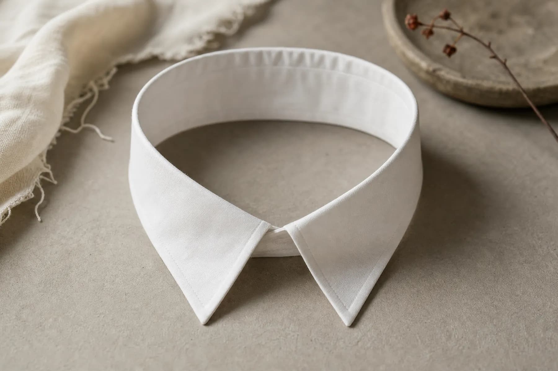 A white cotton shirt collar laid flat on a pale paper ground, its stand upright and the points flat.