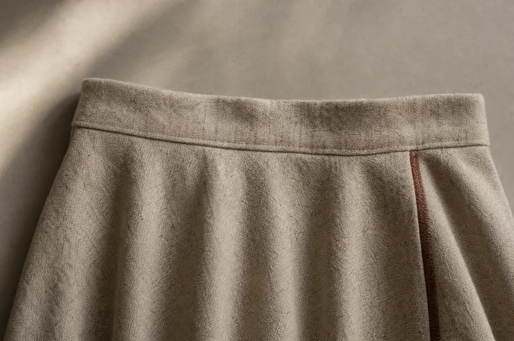 A wool skirt laid flat on a pale paper ground, its waistband running straight across the frame.