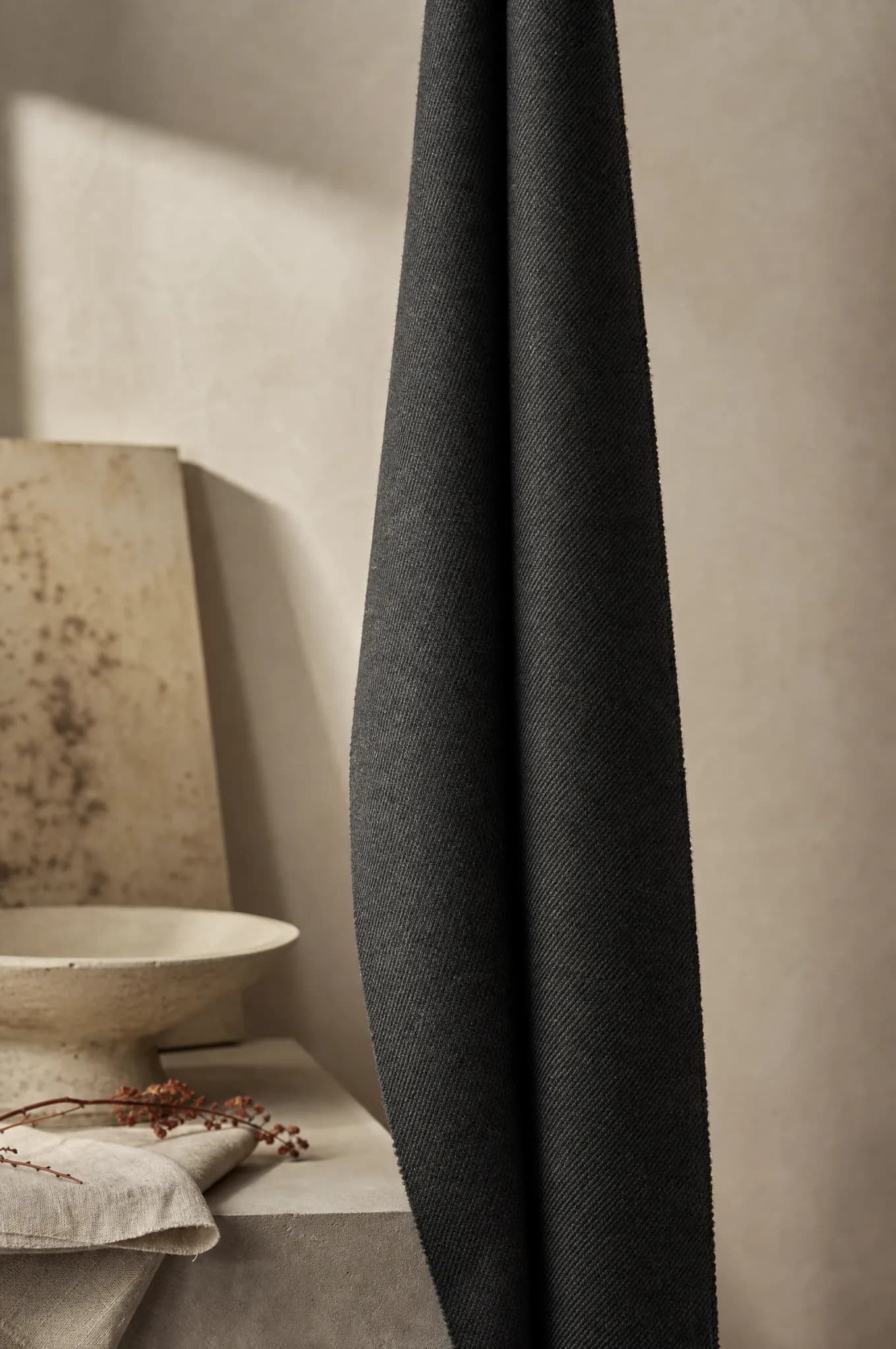 A length of charcoal wool suiting hanging in one long fold, edge-lit.